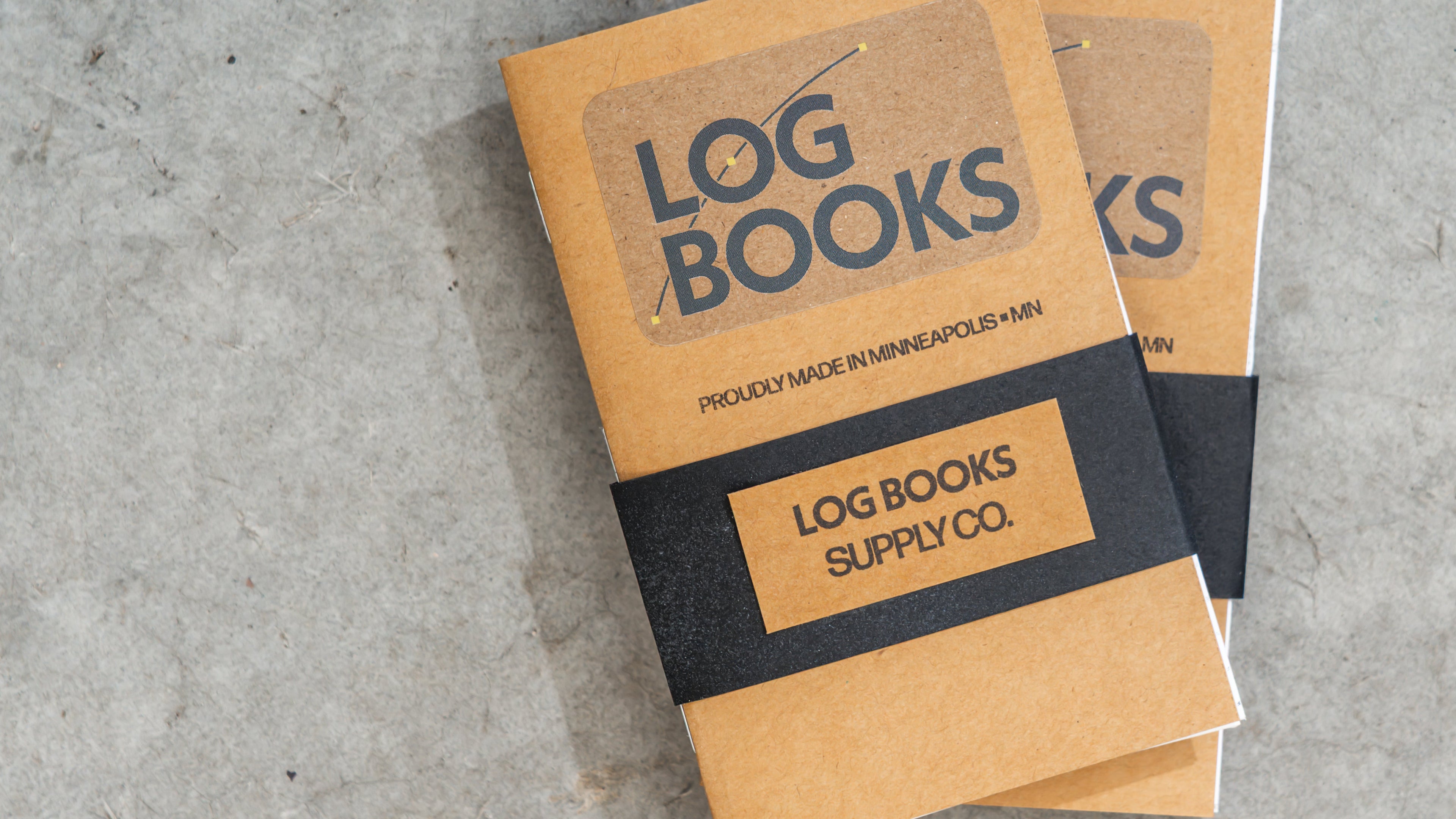 Two log books from Log Books Supply Co. on a concrete surface